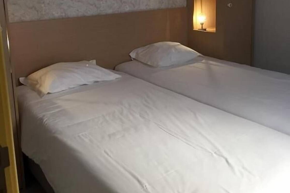 Une chambre d’hôtel avec deux lits, une tête de lit, une lampe fixée au mur et un mur à texture.