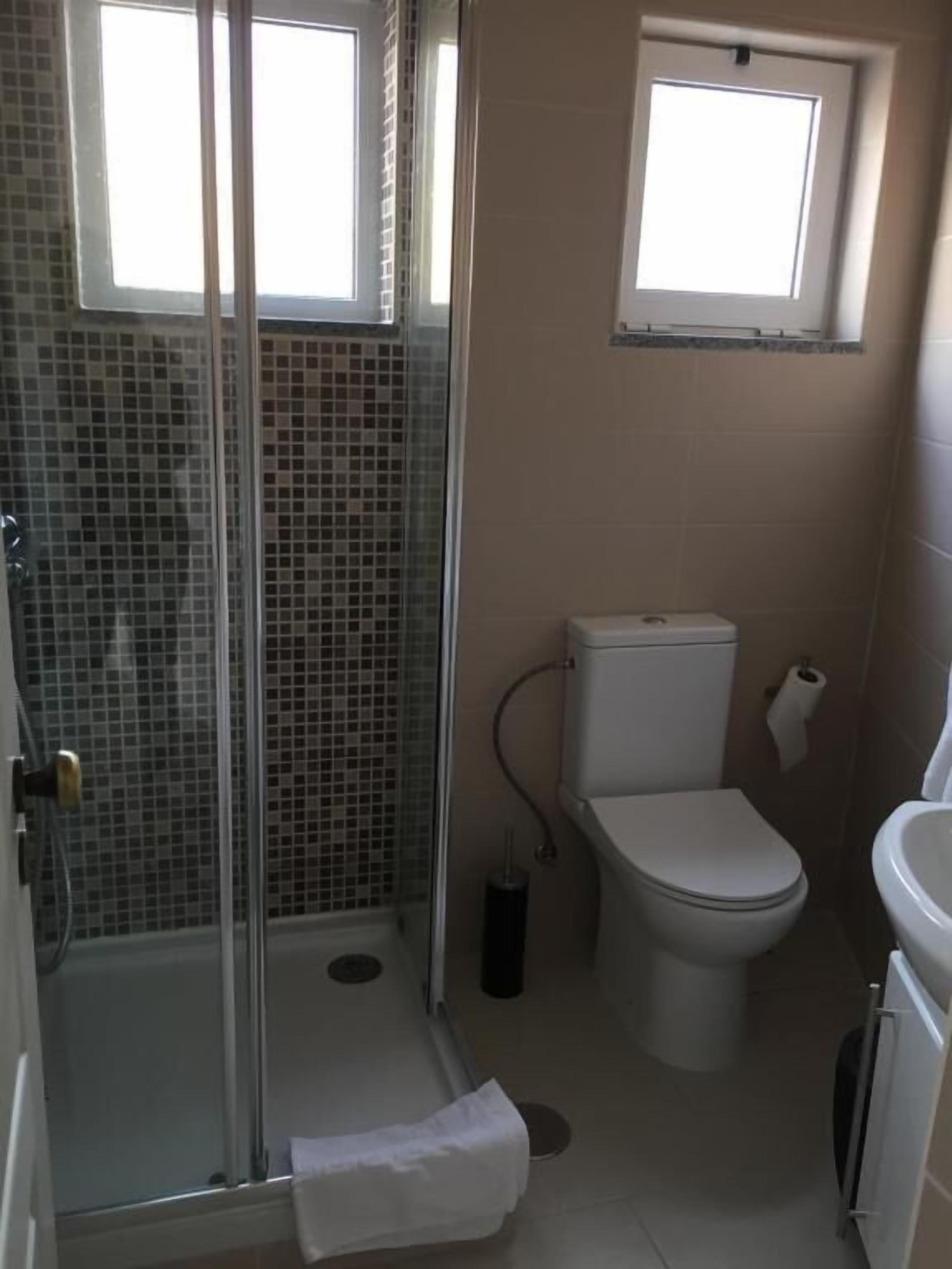 Un baño con cabina de ducha de vidrio, inodoro, lavamanos y ventana sobre el inodoro.