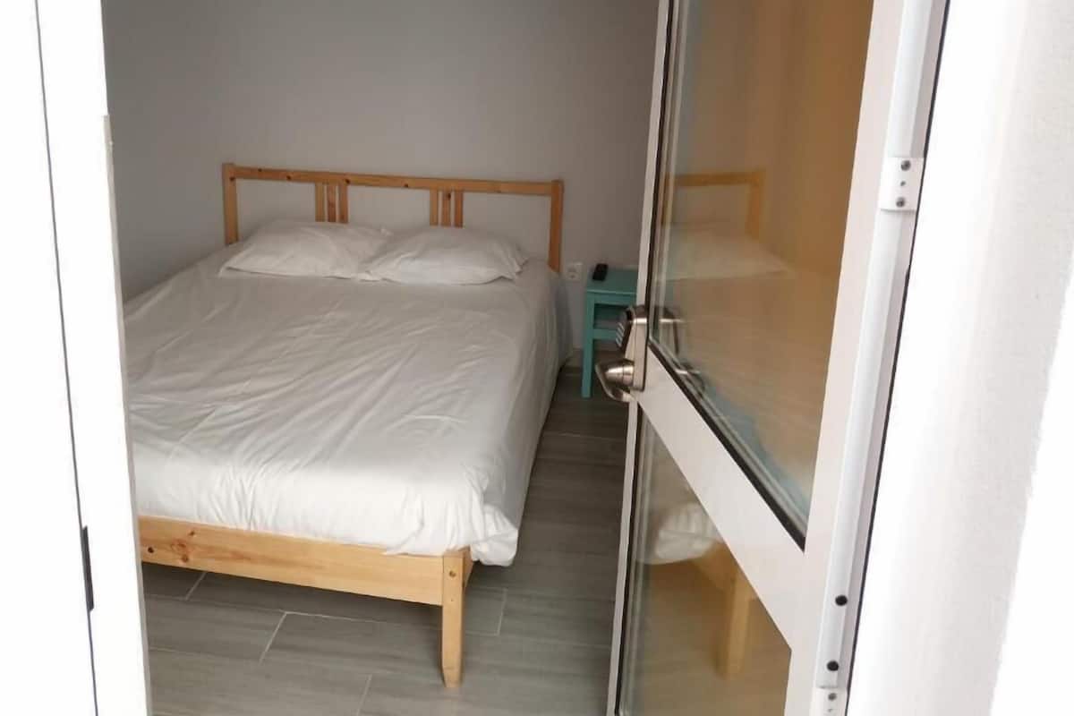 Une chambre à coucher avec un lit en bois, une petite table de chevet et une porte-fenêtre coulissante.