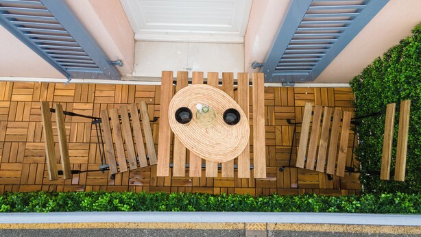 A wooden wall with a circular design, two black circular objects, and a green hedge at the bottom. - DECA CONCIERGERIE (Le Muy)