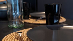 A table set with a black plate, a black cup, a clear glass bottle, and a knife on a woven placemat. - DECA CONCIERGERIE (Le Muy)