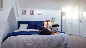Una cama bien hecha con un cabecero azul, ropa de cama blanca y azul, y un plato de fruta a un lado.