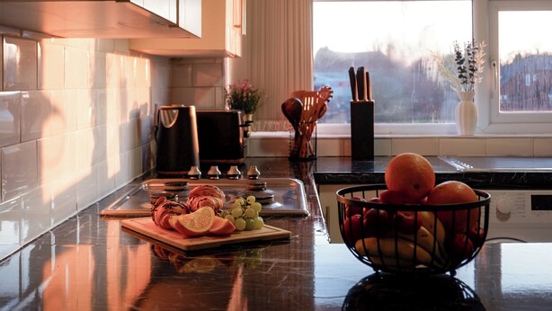 A kitchen with a marble countertop, a cutting board with sliced vegetables, a bowl of fruit, and a window with a view of the outdoors. - Near Uni and Hospital - Long Stays - Fast Wi-Fi - 15 Mins to City (Manchester)