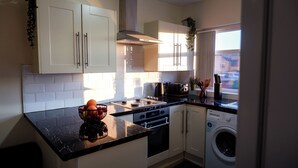 A modern kitchen with white cabinets, a black countertop, a stove, an oven, and a washing machine. - Near Uni and Hospital - Long Stays - Fast Wi-Fi - 15 Mins to City (Manchester)