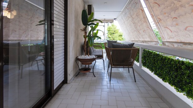 Een overdekt balkon met een bloempot, een rieten stoel en een kleine tafel.