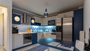 Een moderne keuken met een blauw aanrecht, roestvrijstalen apparatuur en een klok aan de muur.