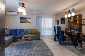 Un salon moderne avec un canapé gris, une table basse et un coin repas comprenant des chaises bleues et une table en verre.