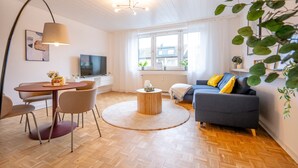 A modern living room with a round coffee table, a sofa, a TV, and a dining area with chairs and a table. - New Apartment, 5 Minutes to Centro and Gasometer (Oberhausen)