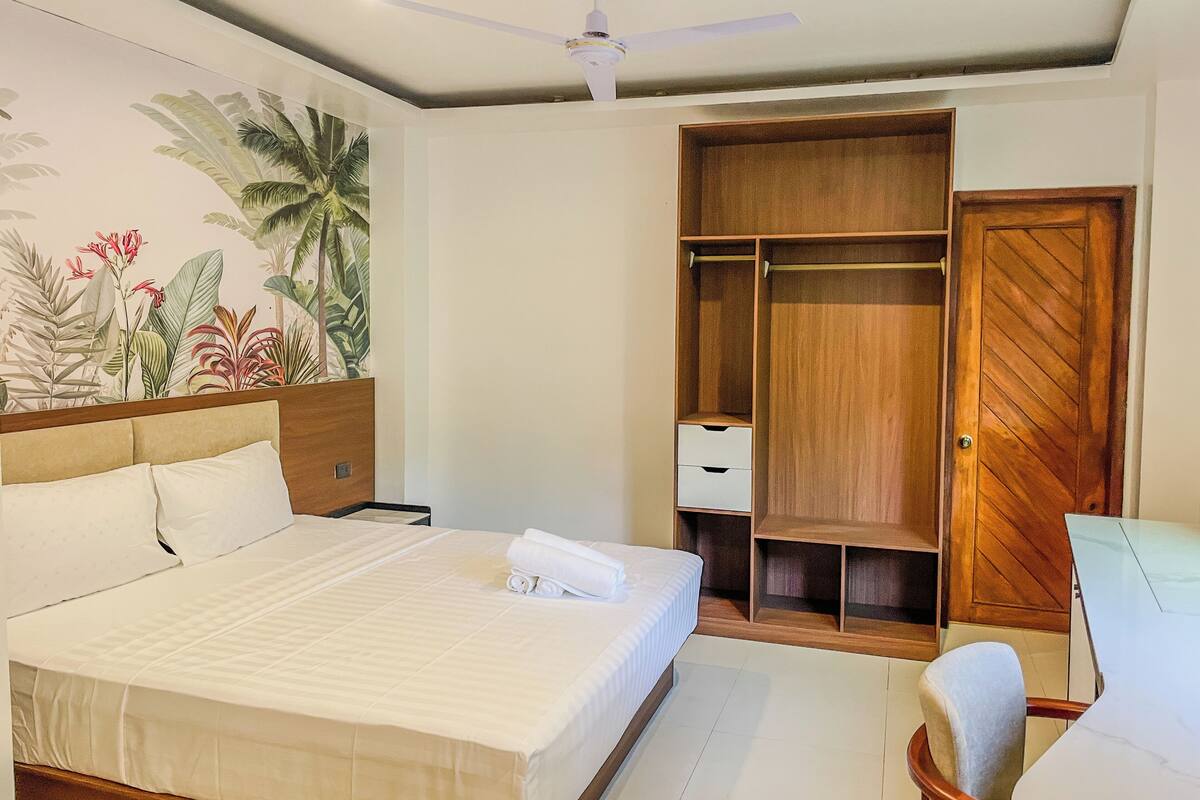 Una habitación de hotel con una cama, un armario, una silla y un ventilador de techo.