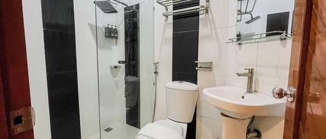 Un baño con cabina de ducha de vidrio, inodoro y lavamanos.