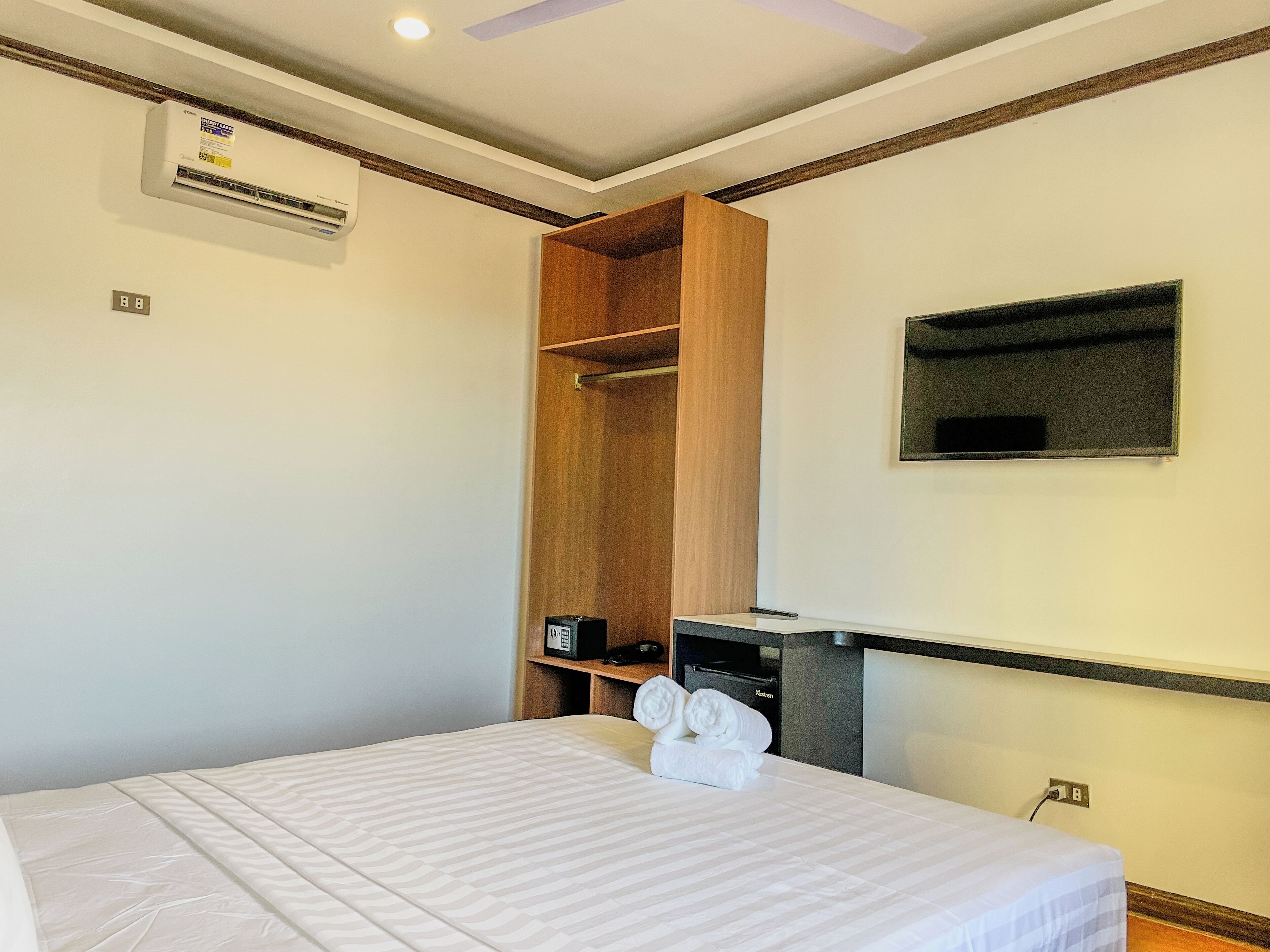 A hotel room with a bed, a wooden wardrobe, a TV, and a minibar.