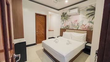 Une chambre d’hôtel avec un lit, une porte en bois, un appareil de climatisation et une fresque murale sur le thème des tropiques.