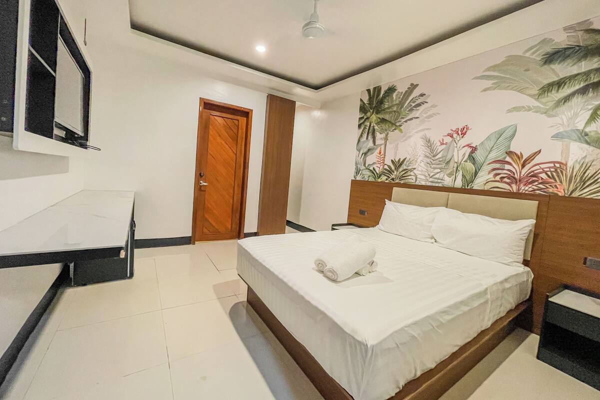 Habitación de hotel con una cama, un escritorio, una puerta y una pared con un mural tropical.