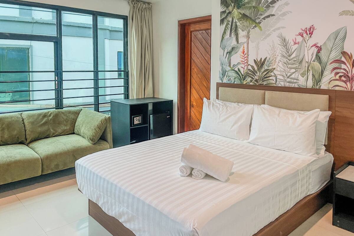 Una habitación de hotel con cama, sofá, un archivador pequeño y una ventana con cortinas.