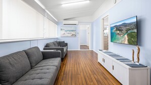 Een modern interieur met een houten vloer, grijze banken, een flatscreen televisie en een schilderij van een kustlandschap.
