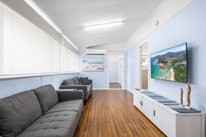 Ein modernes Interieur mit Holzboden, grauen Sofas, einem Flachbildfernseher und einem Gemälde mit einer Küstenansicht.