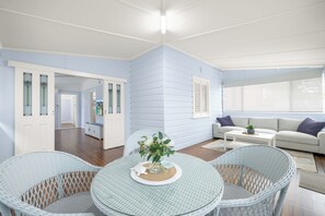 Ein Zimmer mit einem runden Glastisch, Korbstühlen, einer Couch und Blick durch ein Fenster.