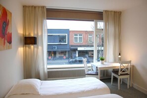A hotel room with a bed, a desk, and a chair. There is a window with a view of the street and buildings outside. - Central-Day Inn (Enschede)