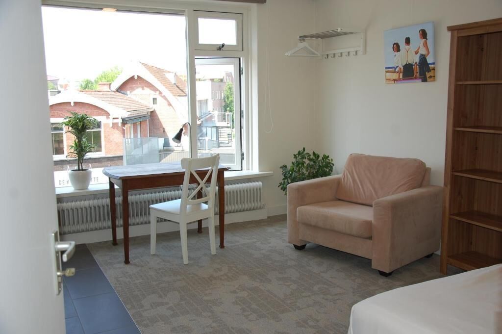 A room with a dining table, a chair, a sofa, a radiator, a window, and a plant.