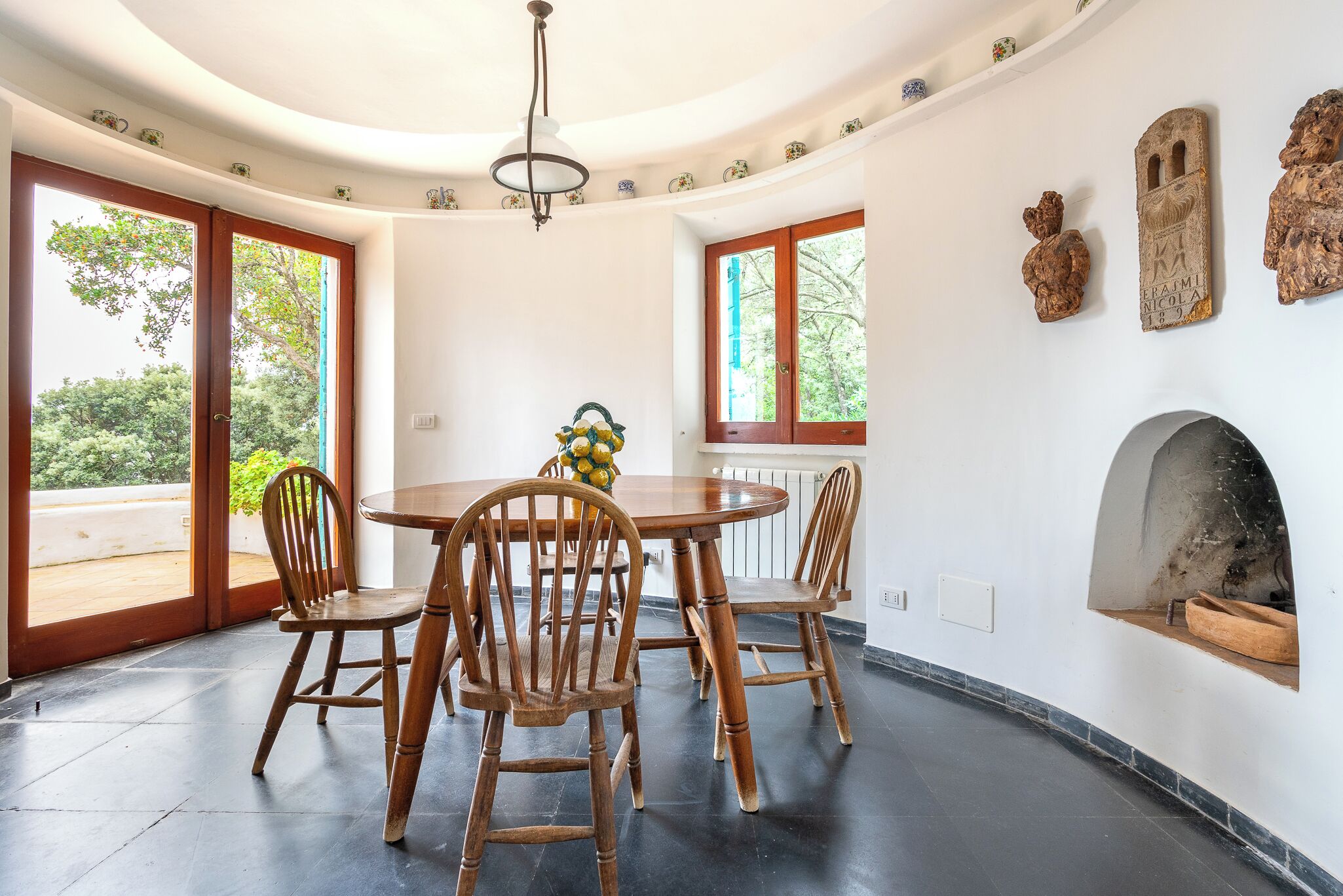 Un comedor con una mesa redonda y sillas de madera, ventanas amplias y una chimenea.