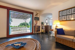 A spacious living area with a wicker sofa, a wicker chair, a dining table with chairs, a glass coffee table, and a large window with a view of the outdoors. - Relax e Natura a Punta Rossa (San Felice Circeo)
