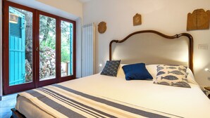 A bedroom with a large bed, a wooden headboard, and a view through a glass door to an outdoor area with a stone wall and greenery. - Relax e Natura a Punta Rossa (San Felice Circeo)