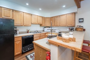 A kitchen with wooden cabinets, a black refrigerator, a dishwasher, a sink, and a small island with stools. - Riverside Condos D02 2 Bedroom Condo (Telluride)