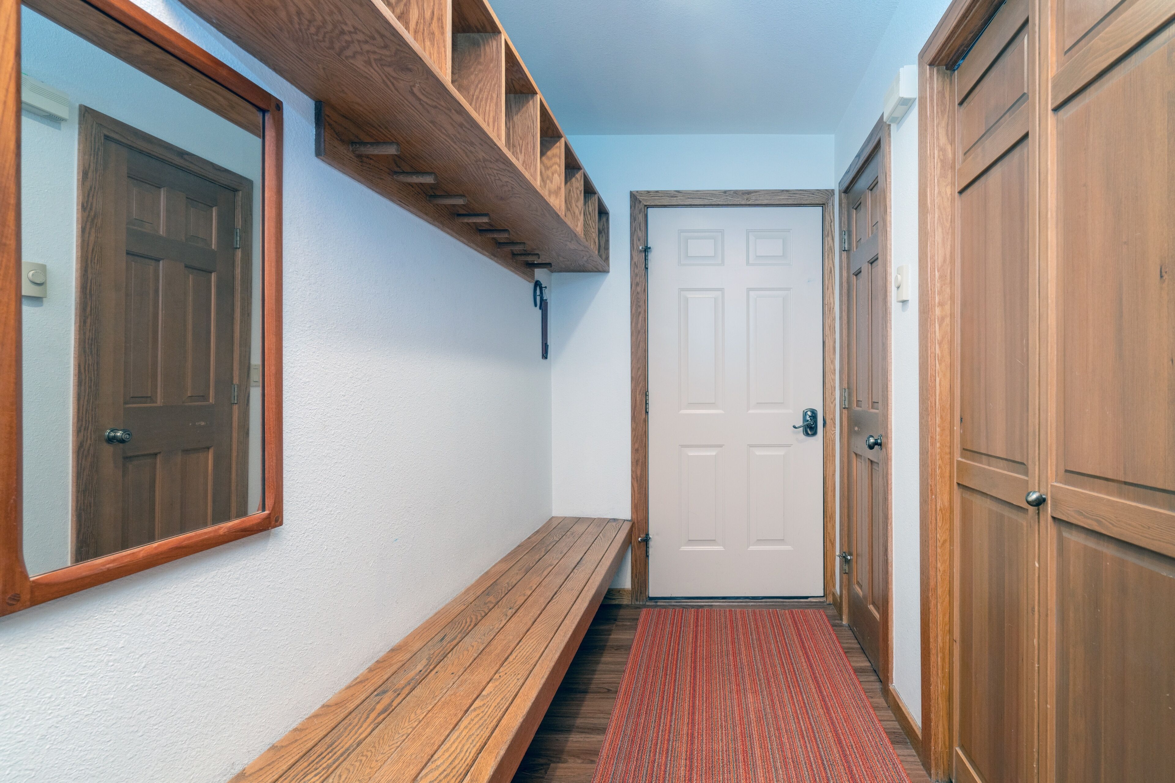 Un couloir avec un banc en bois, une moquette rouge et une porte blanche.