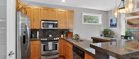 A modern kitchen with wooden cabinets, stainless steel appliances, granite countertops, and a view of the outdoors.