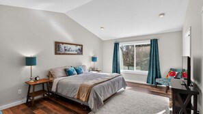 Une chambre à coucher comprenant un lit, deux tables de chevet, un bureau, une chaise, une fenêtre avec des rideaux et un tableau accroché au mur.