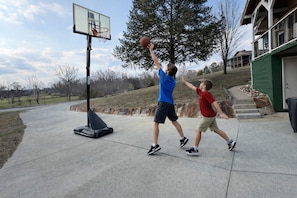 Two children playing basketball on a concrete driveway with a basketball hoop, a house in the background, and a clear sky. - Little Lake Cove 2 Bedroom Home (Sevierville)