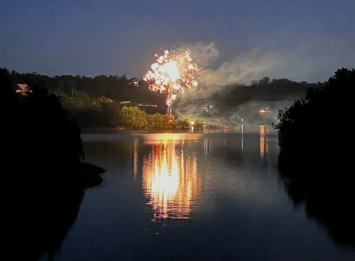A nighttime scene with fireworks over a body of water, reflecting the lights.