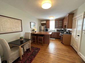 Una cocina con armarios de madera, un comedor con mesa y sillas, y un mapa en la pared.