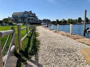 Een pand aan het water met een houten looppad dat naar een steiger leidt, een groot huis met meerdere verdiepingen en een gazon.