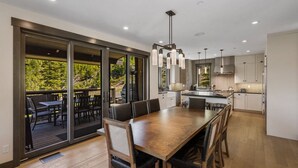 Una cocina moderna con una amplia mesa de comedor, puertas de cristal correderas que dan a un patio exterior y vistas a una zona boscosa.