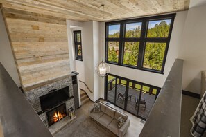 Ein modernes Interieur mit Kamin aus Stein, Holzboden und einem großen Fenster mit Blick auf einen Wald.