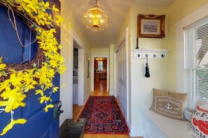 A hallway with a red patterned rug, a blue door with yellow foliage, a hanging light fixture, and a bench with a 'Entering Newport' pillow. - 12 Goodwin Unit 1 1 Bedroom Apts (Newport)