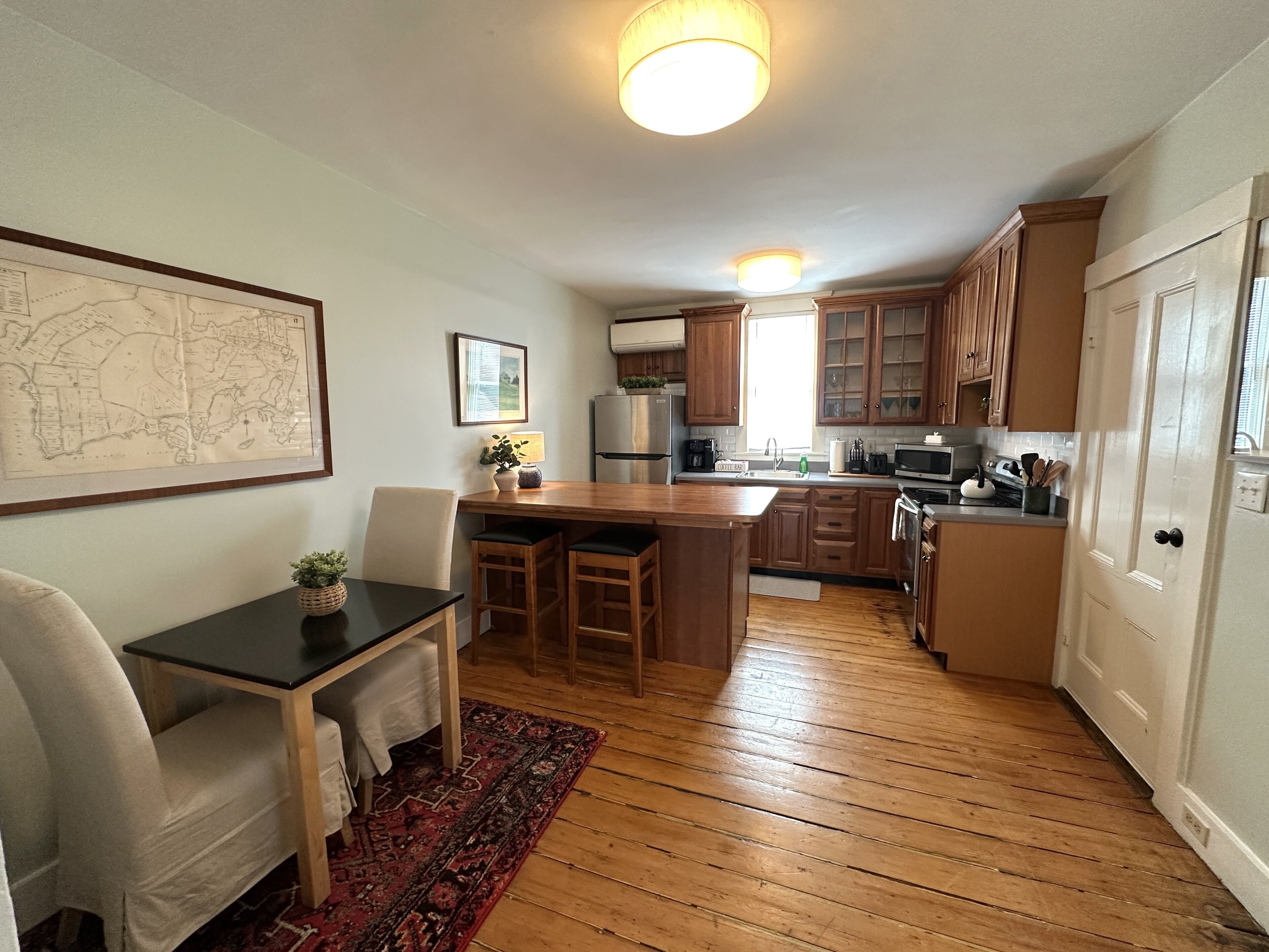 Una cocina con armarios de madera, un comedor con mesa y sillas, y un mapa en la pared.