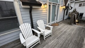 A wooden deck with two Adirondack chairs, a pergola, and a house with a grey exterior and a large arched window. - 12 Goodwin Unit 2 1 Bedroom Apts (Newport)