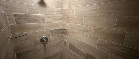 A shower with beige tiles, a glass shelf, and a showerhead.