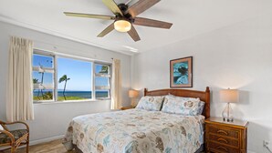 A bedroom with a bed, a nightstand, a chair, a ceiling fan, a window with curtains, and a framed picture on the wall. - Menehune Shores, #524 2 Bedroom Condo (Kihei)