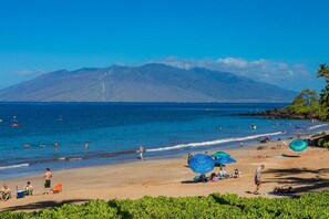 A beach with people swimming and sunbathing, umbrellas, and a mountain in the background. - Polo Beach Club 703 2 Bedroom Condo (Kihei)