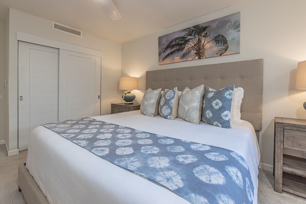 A bedroom with a bed, a headboard, a nightstand, a lamp, a painting, and a wardrobe. - Polo Beach Club 703 2 Bedroom Condo (Kihei)