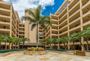 A multi-story hotel with a central courtyard featuring palm trees and a swimming pool. - Polo Beach Club 703 2 Bedroom Condo (Kihei)