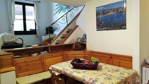 A kitchen with wooden cabinets, a dining table with a floral tablecloth, and a fruit basket. - Villa Claudia Residence I Mandorli (Villaggio Mandorli)