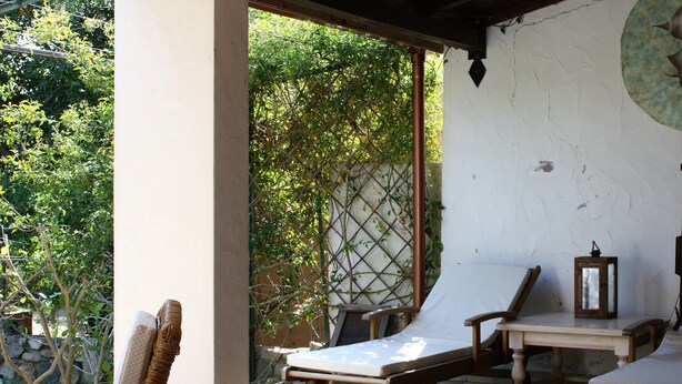 A covered outdoor seating area with wicker chairs, a lounge chair, and a small table. - Villa Claudia Residence I Mandorli (Villaggio Mandorli)