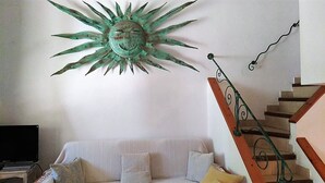 A room with a sun-shaped wall decoration, a staircase with a metal railing, and a sofa with cushions. - Villa Claudia Residence I Mandorli (Villaggio Mandorli)
