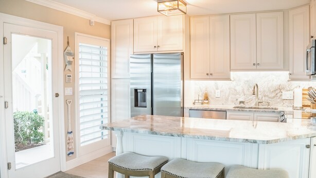 Una cocina con una isla grande, armarios blancos, electrodomésticos de acero inoxidable y vistas al exterior.