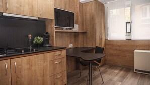 A compact kitchen with wooden cabinets, a built-in stove, a coffee machine, and a small dining area with a chair. - Soothing 1-bedroom studio in charming Stuttgart perfect for your stay W3_P13 (Stuttgart)