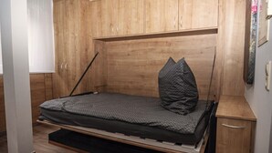 A compact room with a bed, wooden wardrobe, and a small desk with drawers. - Soothing 1-bedroom studio in charming Stuttgart perfect for your stay W3_P13 (Stuttgart)